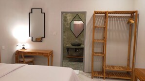 Un dormitorio con cama, escritorio, espejo, armario de madera y baño con lavamanos y espejo.