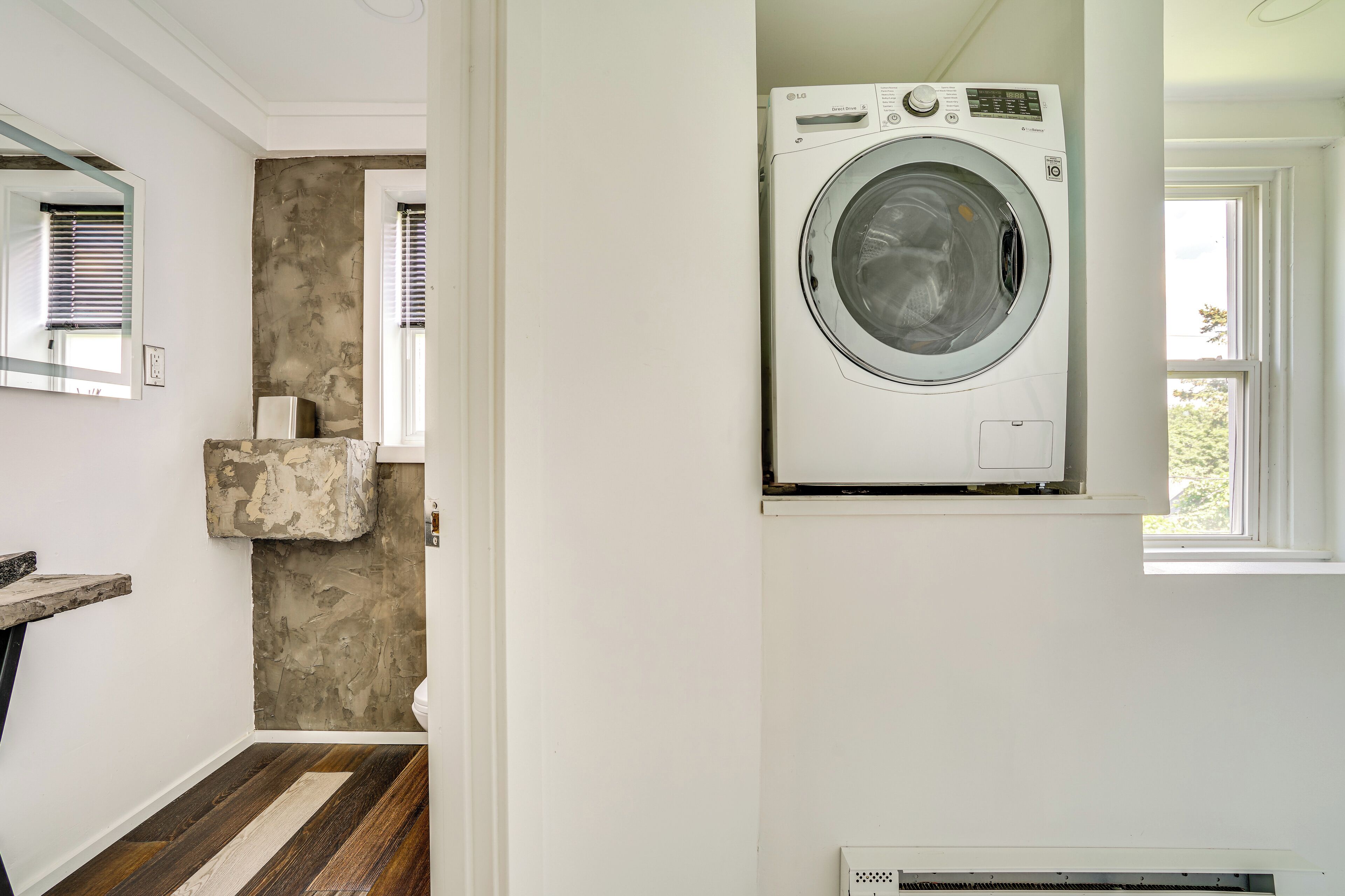 Une buanderie équipée d’un lave-linge, avec un mur d’accent en pierre et une fenêtre.