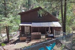 A cabin with a porch, a hot tub, and a fenced outdoor area with chairs. - Quiet Cabin Retreat: Minutes from Cloudcroft! (Cloudcroft)