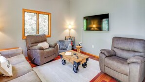 A living room with a sofa, a recliner, a coffee table, a lamp, and a television mounted on the wall. - Quiet Cabin Retreat: Minutes from Cloudcroft! (Cloudcroft)