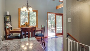 A dining area with a wooden table, chairs, and a chandelier. There are windows with a view of trees and a sliding glass door leading to an outdoor area. - Quiet Cabin Retreat: Minutes from Cloudcroft! (Cloudcroft)