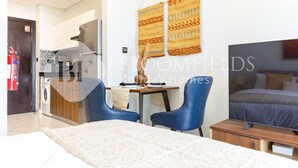 Une chambre d’hôtel moderne équipée d’un lit, d’un bureau, de deux chaises, d’un coin cuisine et d’un extincteur.