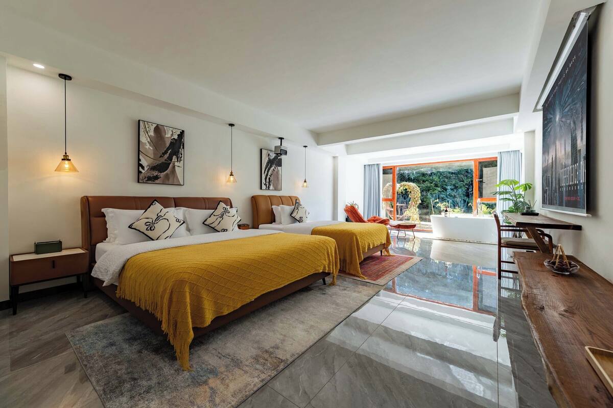 Quarto moderno com duas camas, uma escrivaninha de madeira e uma janela grande.