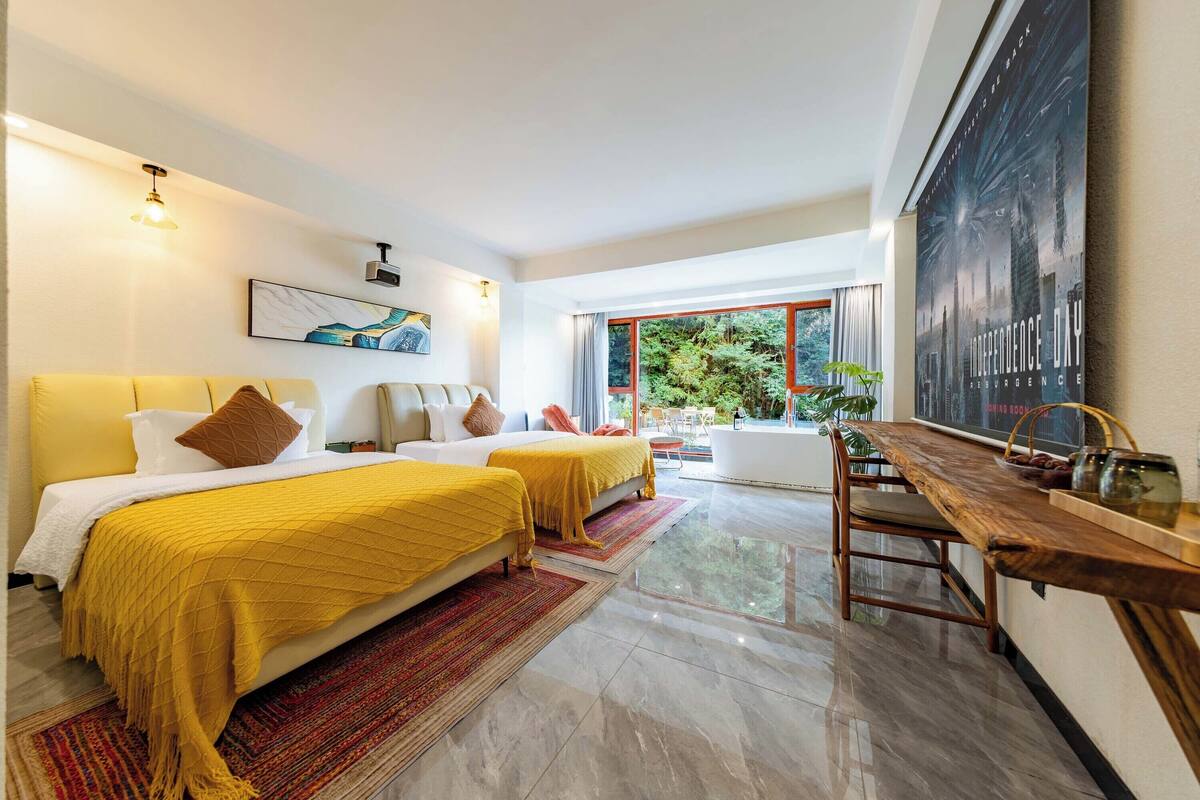 Quarto de hotel moderno com duas camas, uma mesa de jantar de madeira e uma grande janela com vista para o verde.