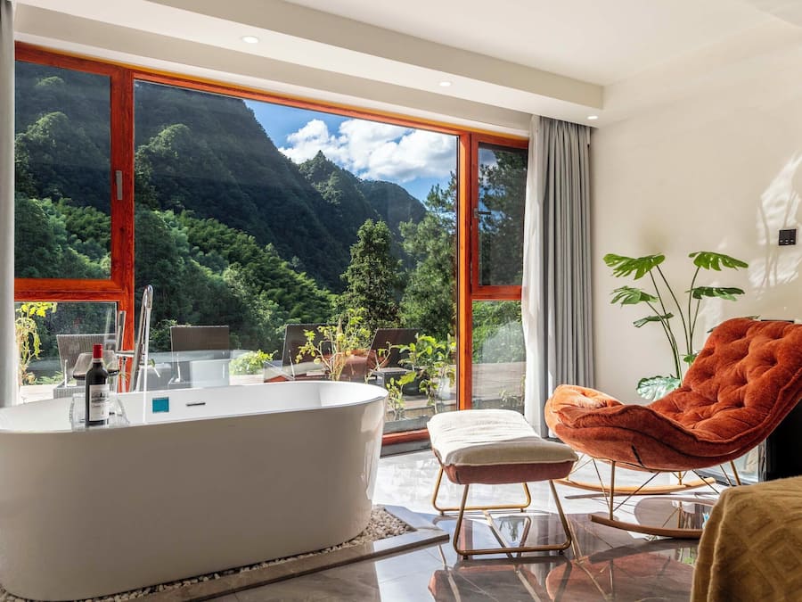 Un baño moderno con una bañera independiente, un sillón tapizado en rojo y un ventanal con vistas a la montaña.