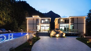 A modern two-story building with a swimming pool, surrounded by a landscaped garden and a mountain backdrop. - Huagu Jianzhu Guesthouse Zhangjiajie (Zhangjiajie)