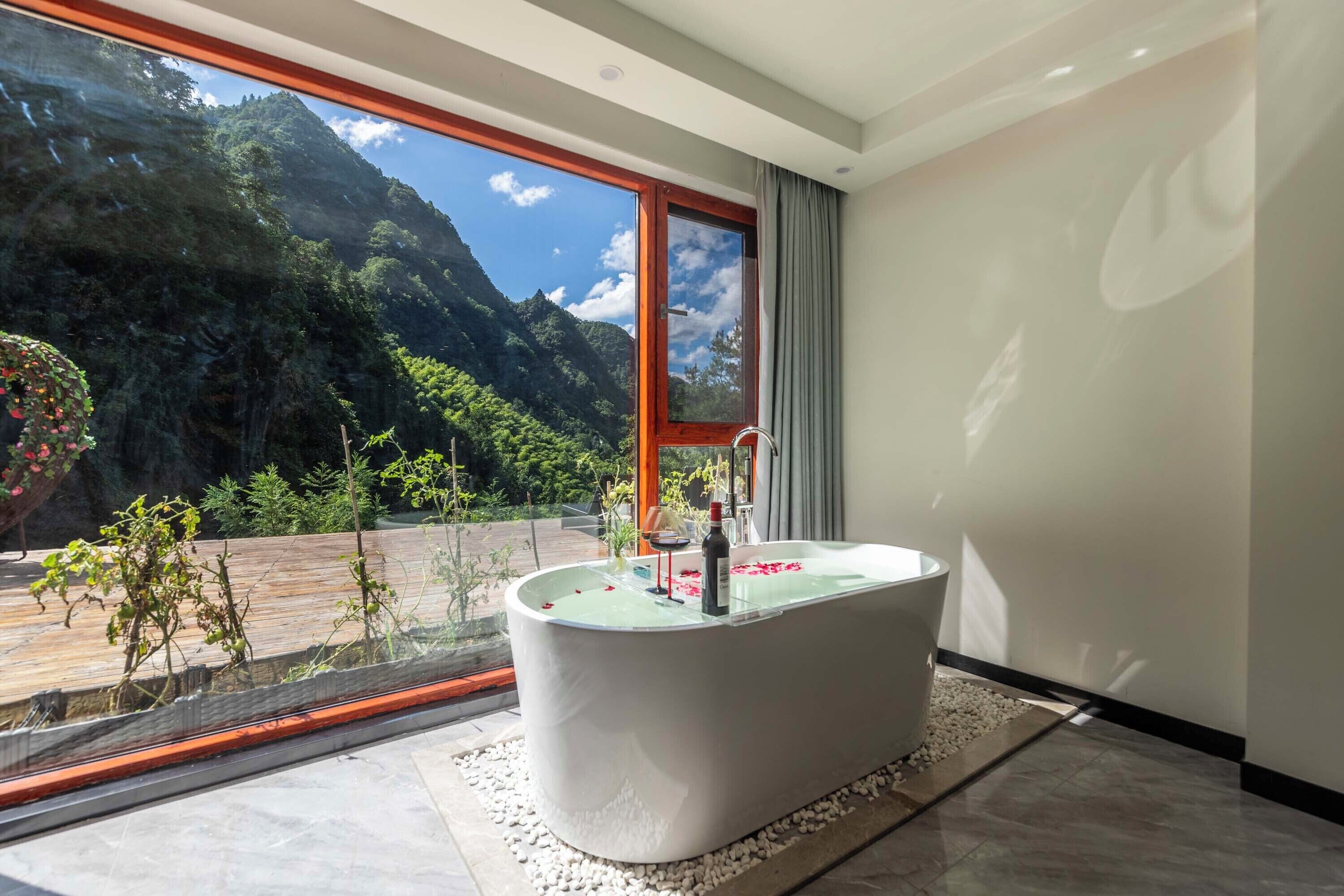 A modern bathroom with a freestanding bathtub, a large window with a mountain view, and a glass shower enclosure.