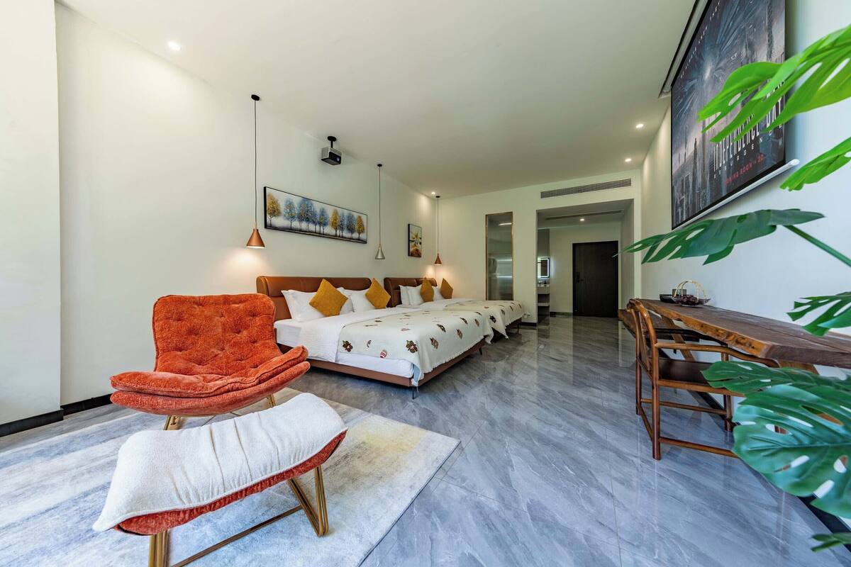 Quarto de hotel moderno com uma cama grande, área de estar com uma poltrona e uma mesa, e uma mesa de jantar.