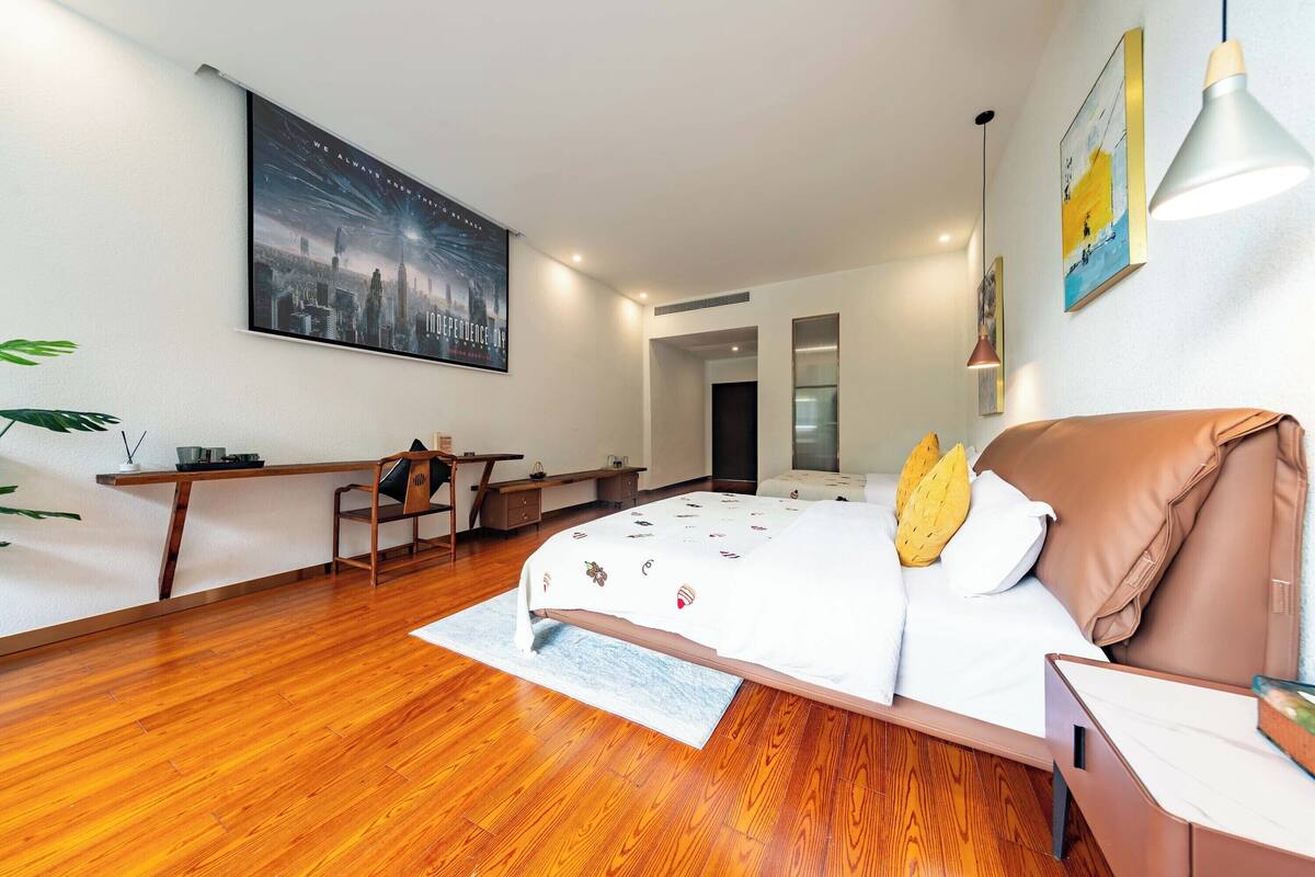 Um quarto moderno com piso de madeira, uma cama com colcha estampada, uma escrivaninha com cadeira e um pôster grande de um horizonte urbano na parede.