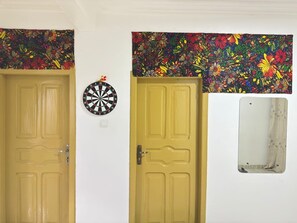 Deux portes recouvertes d’un papier peint à motifs floraux, un jeu de fléchettes et un miroir.