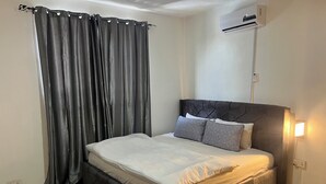 Une chambre à coucher avec un lit, des rideaux gris, un appareil de climatisation et une lampe de chevet.