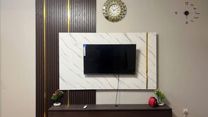 Un salon moderne avec un téléviseur fixé au mur, une horloge murale et une horloge décorative également fixée au mur.