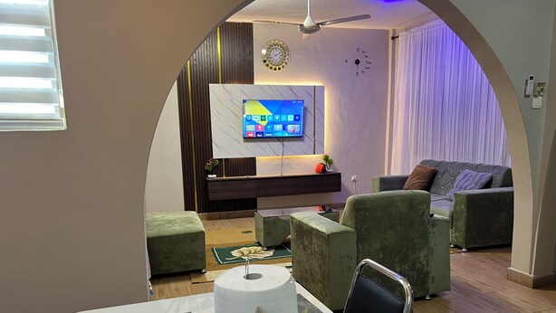Un salon moderne doté d’un téléviseur à écran plat, de fauteuils à revêtement vert, d’une table à manger avec un plateau en marbre et d’une plante décorative.