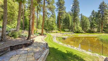 A stone pathway leading to a pond surrounded by tall trees.