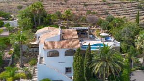Une villa blanche avec un toit en tuiles, une piscine et une végétation luxuriante.