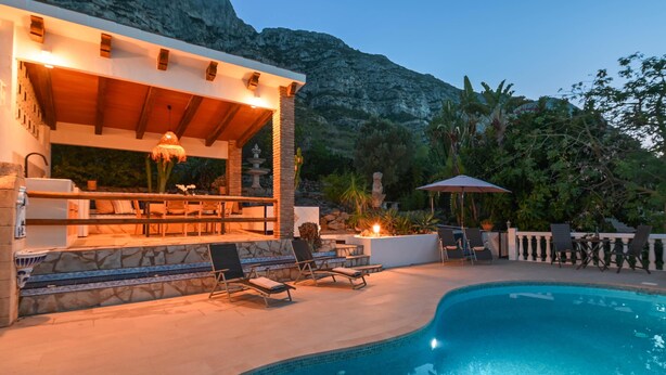 Un espace aménagé au bord de la piscine, comprenant un bar, des chaises longues et offrant une vue sur les montagnes.