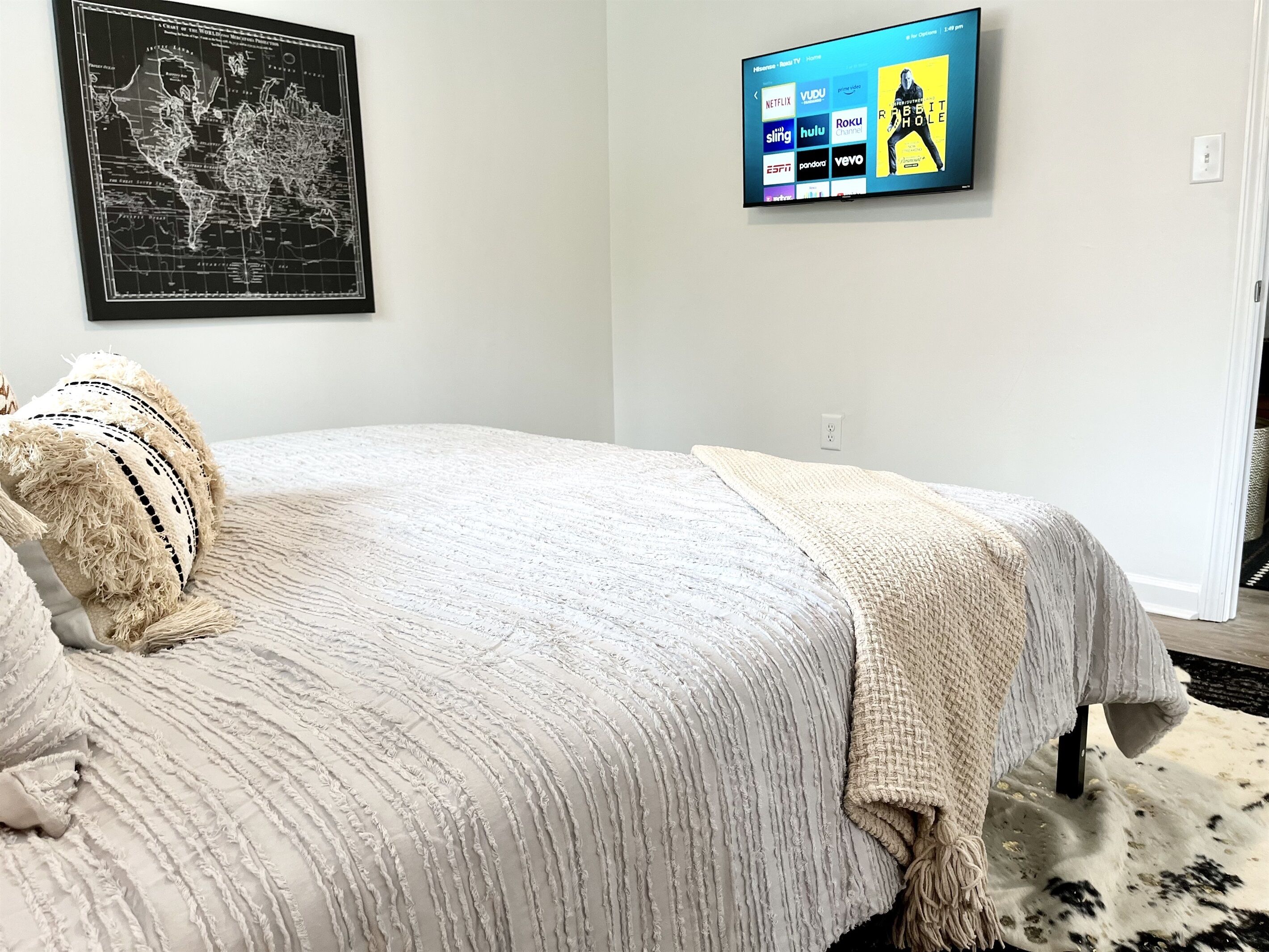 Ein Schlafzimmer mit einem Bett, einem an der Wand montierten Fernseher, der Streamingdienste anzeigt, und einer Weltkarte an der Wand.