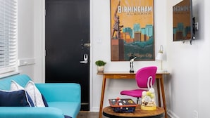 A room with a black door, a blue sofa, a wooden side table with a lamp, and a poster of Birmingham, Alabama. - The Vulcan Octoplex - 8 Private Units/WiFi/Parking (Birmingham)