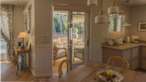 Un comedor con una mesa de madera, sillas, un cuenco de fruta y una encimera de cocina con electrodomésticos.