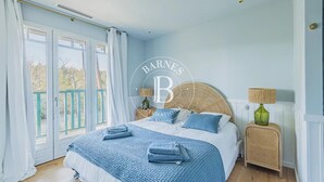 Un dormitorio con una cama grande, una mesita de mimbre y vistas al exterior a través de una puerta corredera.