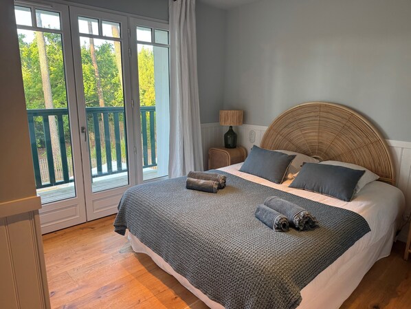 A bedroom with a large bed, a wicker headboard, a view through a sliding glass door to a balcony, and a nightstand with a lamp.