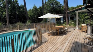 Una terraza de madera con piscina, rodeada por una valla de bambú y árboles.