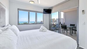 A hotel room with a large bed, a TV mounted on the wall, and a balcony with a table and chairs. - Stylish 1-Bed Darwin City Stay with Balcony Views (Darwin City)
