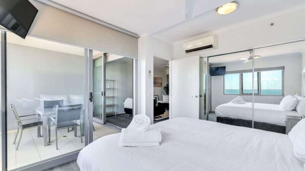 A modern hotel room with a large bed, a desk, and a glass door leading to a balcony. - Stylish 1-Bed Darwin City Stay with Balcony Views (Darwin City)