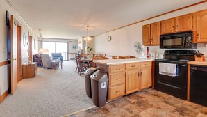 A spacious kitchen with wooden cabinets, a black microwave, and a large island. There is a dining area with a table and chairs in the background. - Mtn Views & Pool Access: Lake Memphremagog Condo! (Newport)