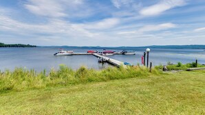 A lakeside dock with boats and a grassy shoreline. - Mtn Views & Pool Access: Lake Memphremagog Condo! (Newport)