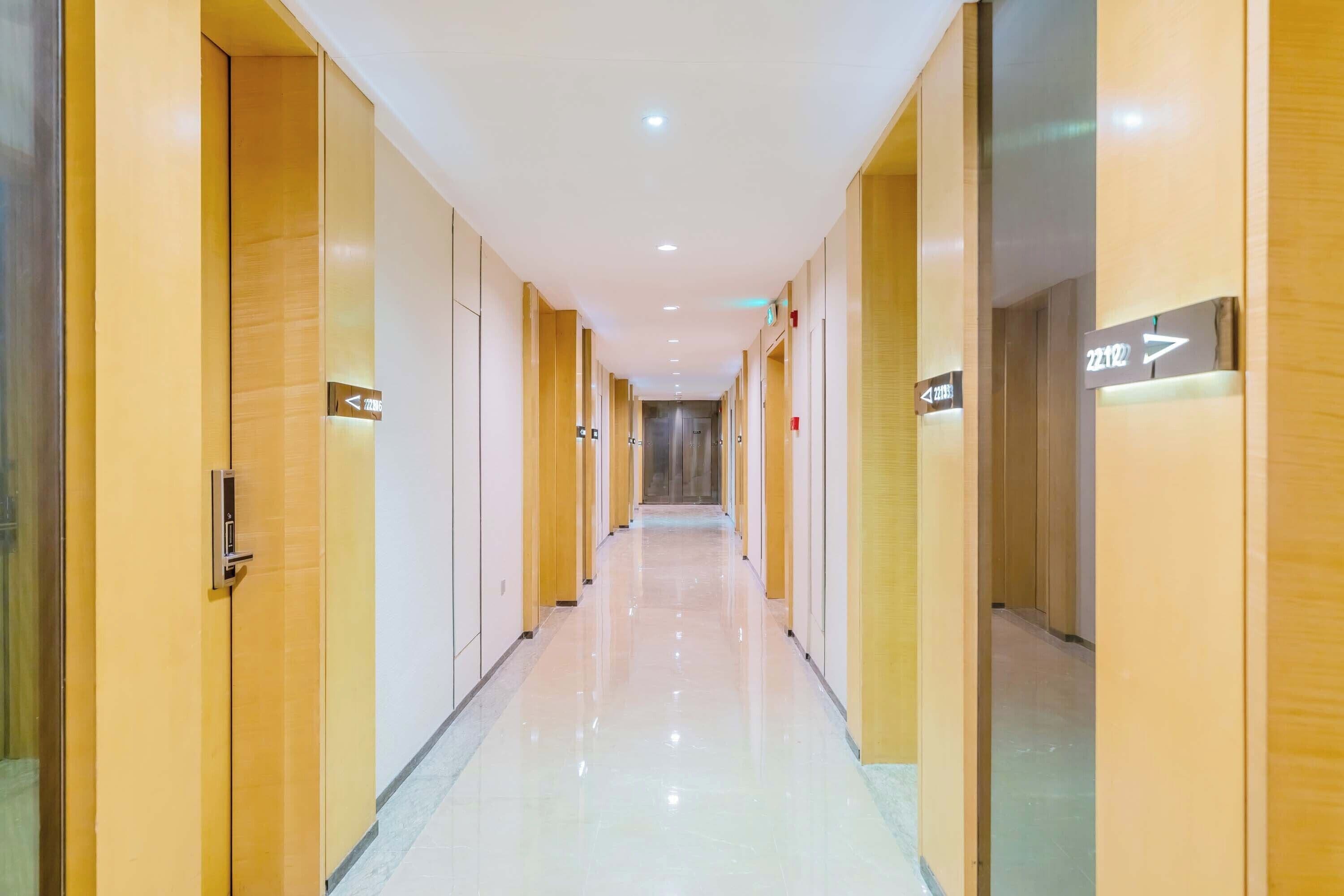 A long, well-lit hallway with doors marked with room numbers and directional arrows.