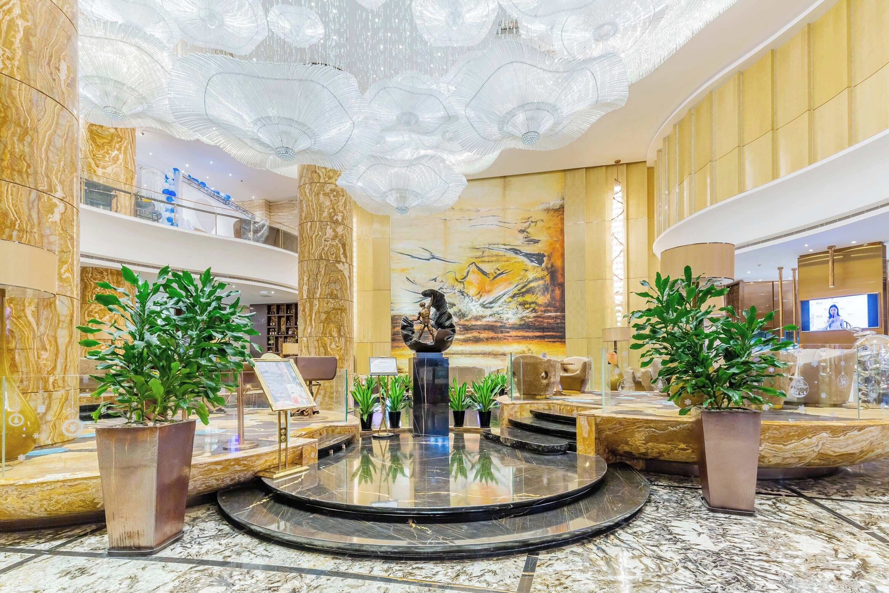 A lobby with a marble floor, a central sculpture, and potted plants.