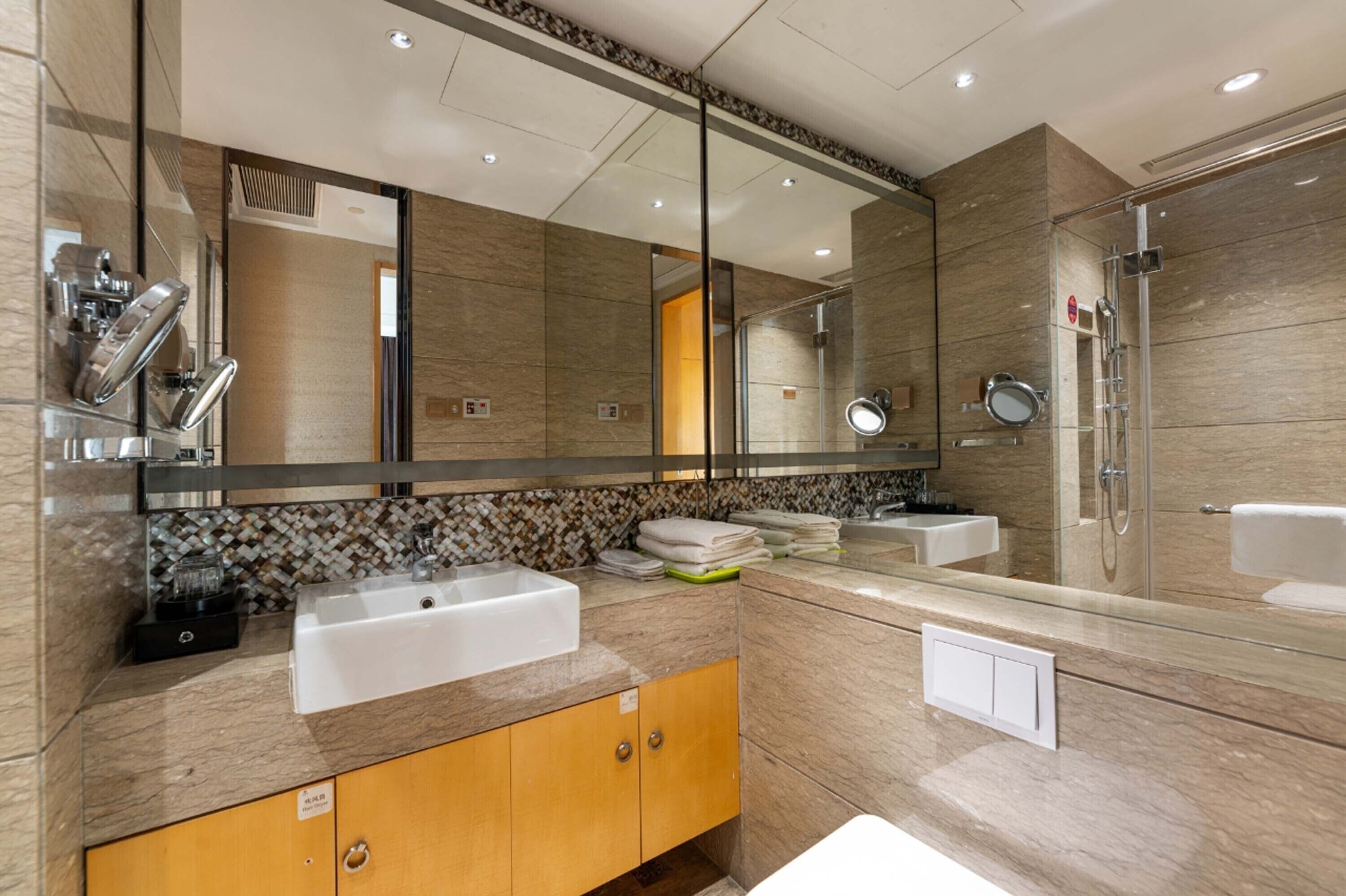 A modern bathroom with a large mirror, two sinks, a shower, and a vanity with a towel rack.