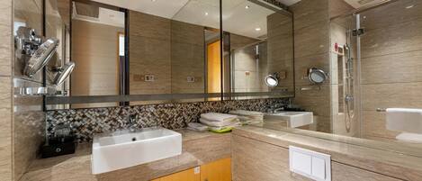 A modern bathroom with a large mirror, two sinks, a shower, and a vanity with a towel rack.