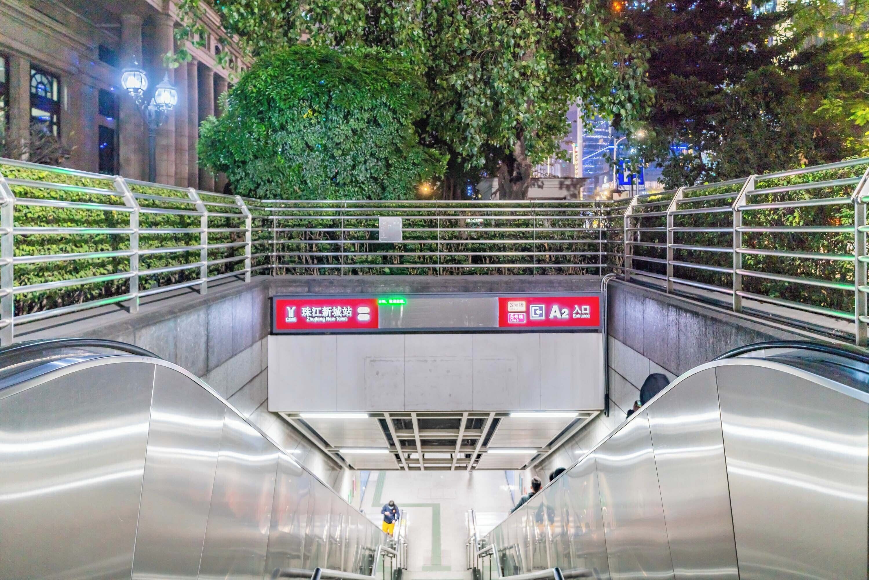 An indoor escalator with metal railings and a green tree in the background.
