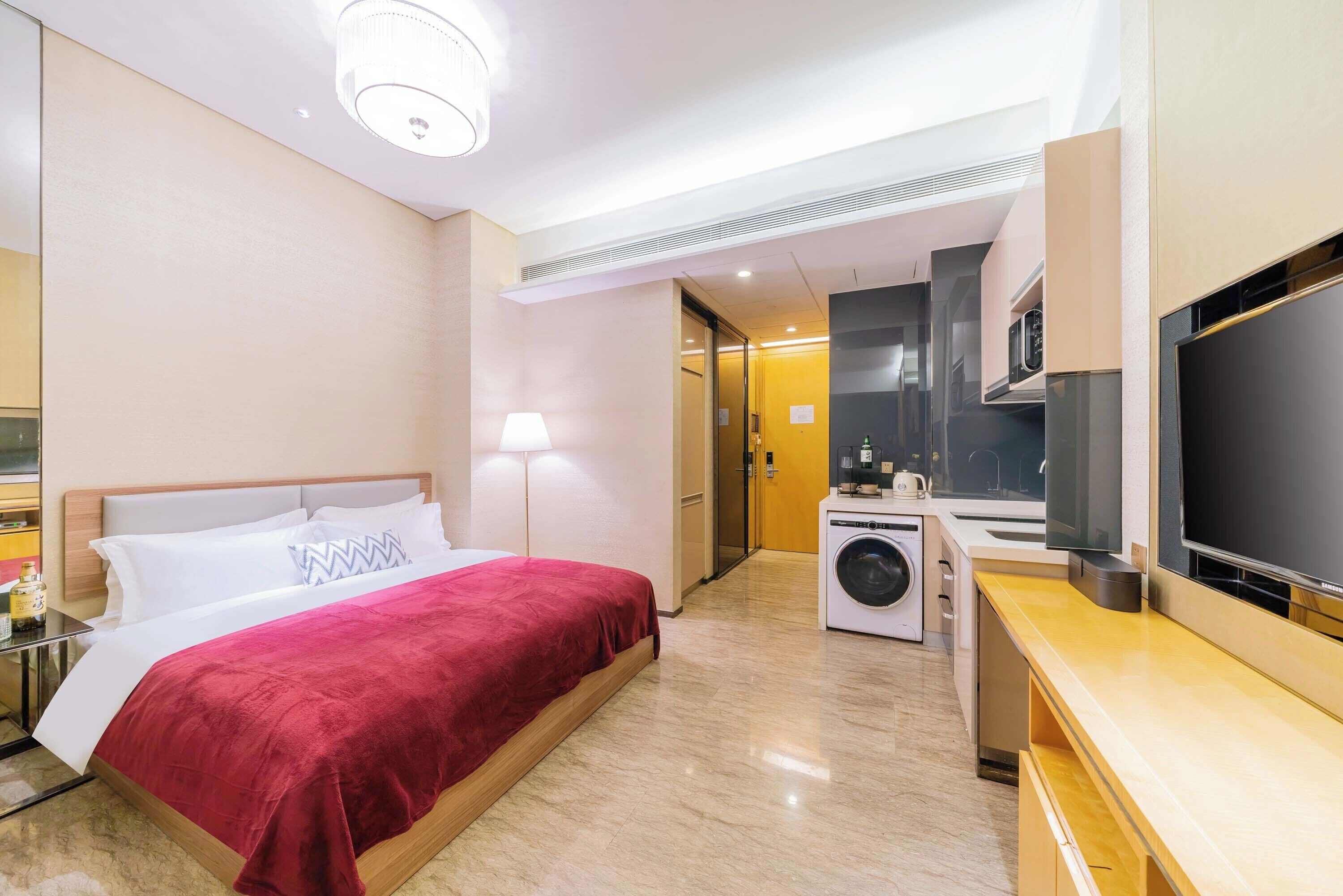 A hotel room with a bed, a washing machine, a TV, and a small kitchenette.