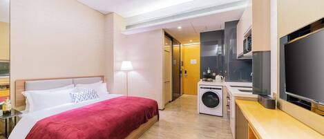 Ein Hotelzimmer mit einem Bett, einer Waschmaschine, einem Fernseher und einer kleinen Küchenzeile.