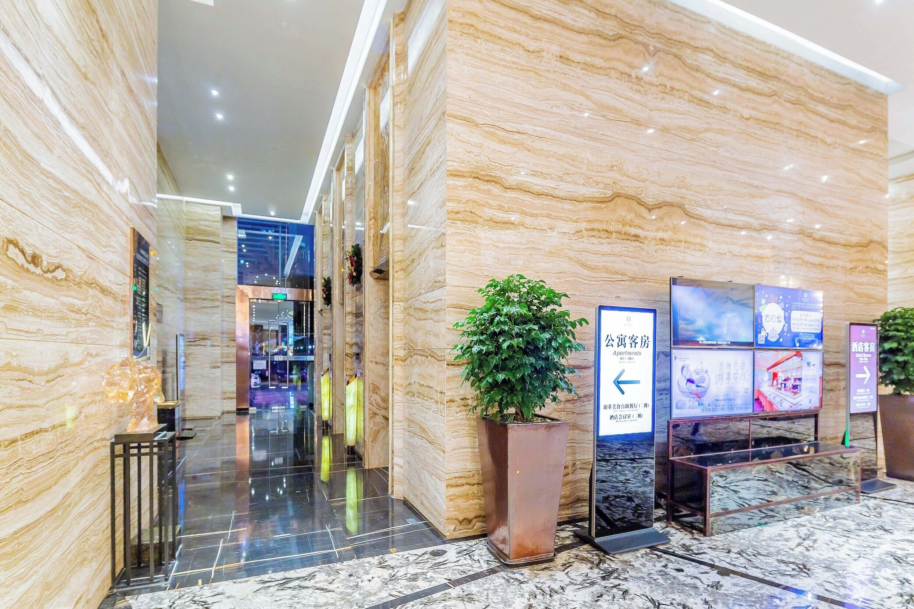 A hotel lobby with marble walls, a potted plant, and directional signs.