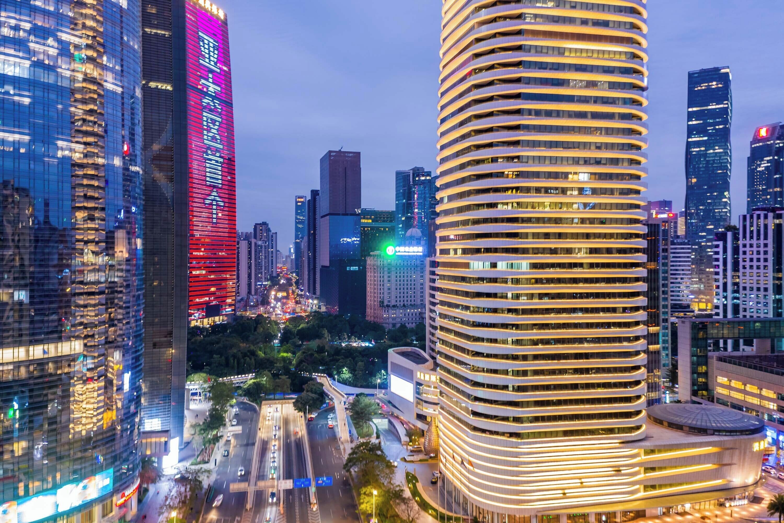 A modern high-rise building with a curved facade and illuminated windows, surrounded by other skyscrapers and busy streets.