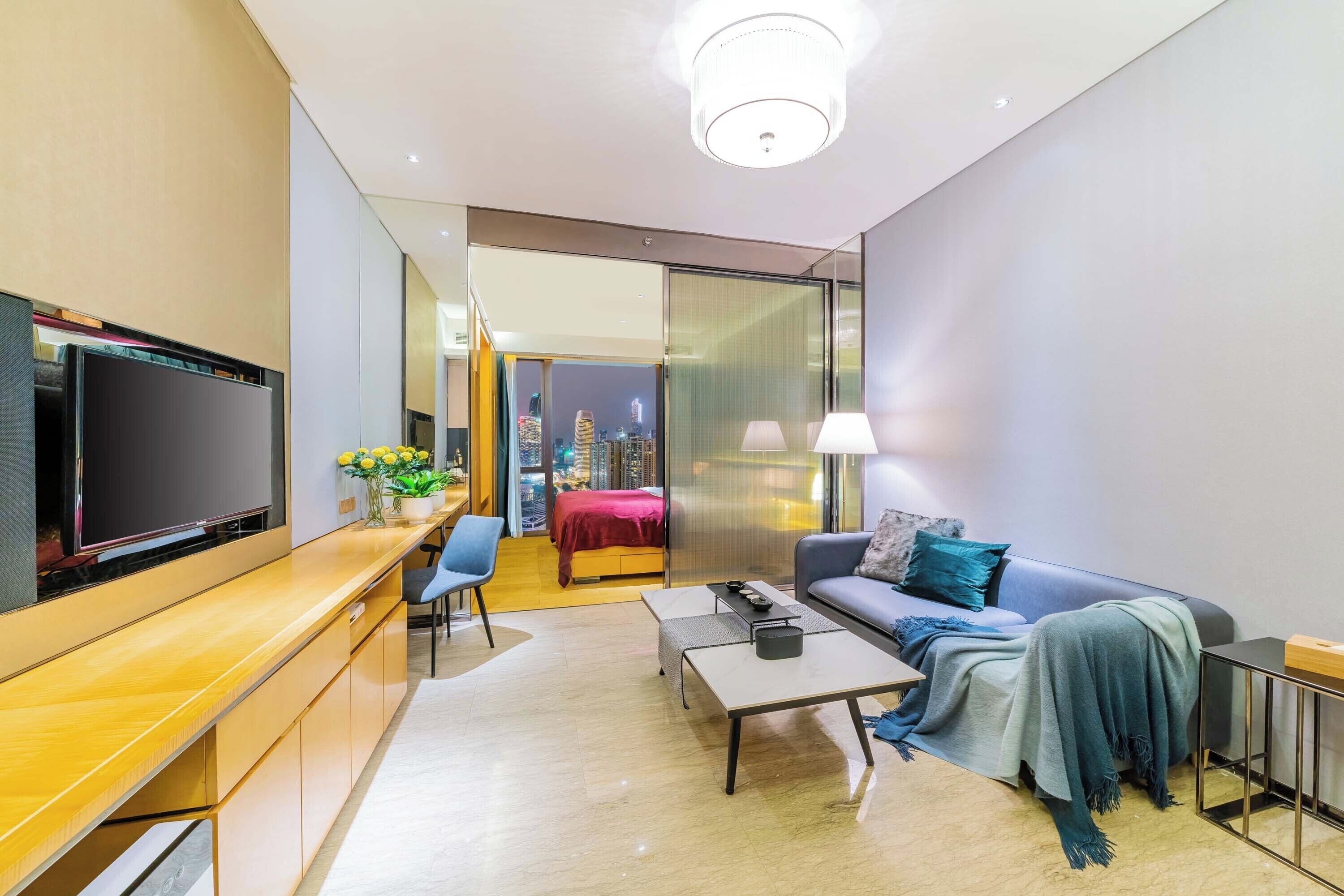 Una habitación de hotel moderna con una televisión de pantalla plana, un sofá, una mesa de centro, un escritorio y vistas de la ciudad a través del ventanal.