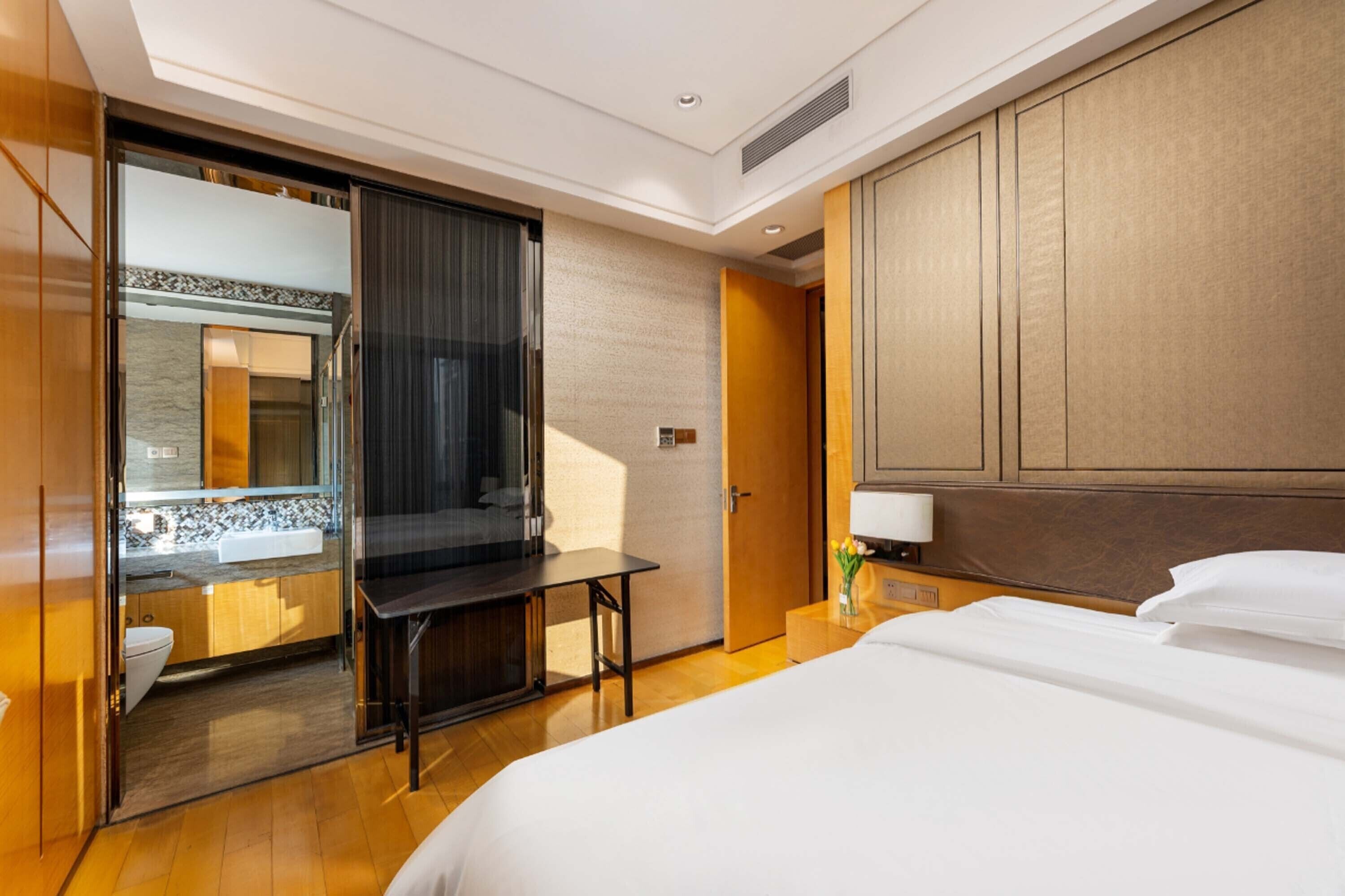 Une chambre d’hôtel comprenant un lit, un bureau, un miroir, une salle de bain avec un lavabo et des toilettes, et une tête de lit en bois.