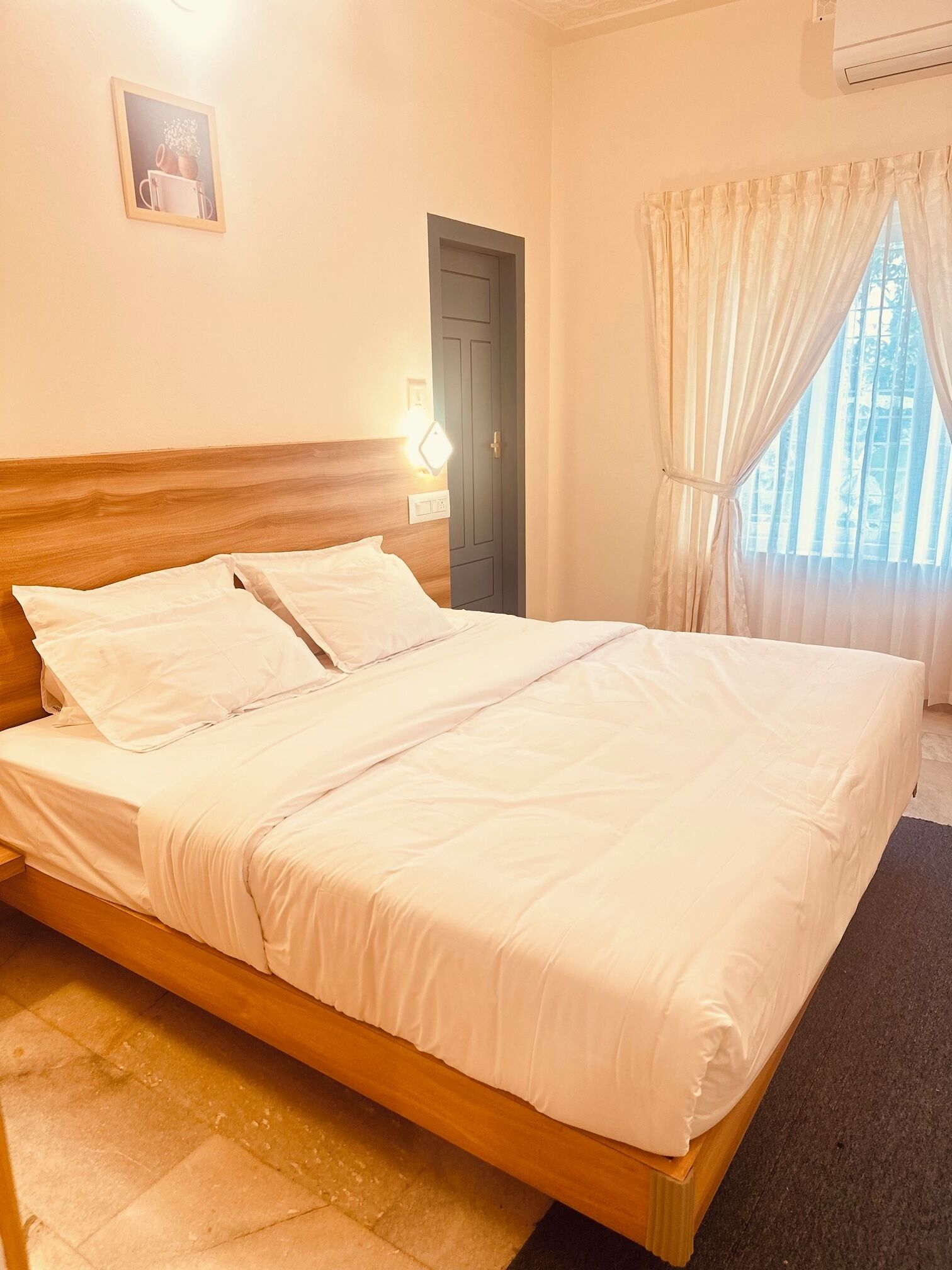 Una cama bien hecha con sábanas blancas en una habitación con cabecera de madera, una puerta y una ventana con cortinas.