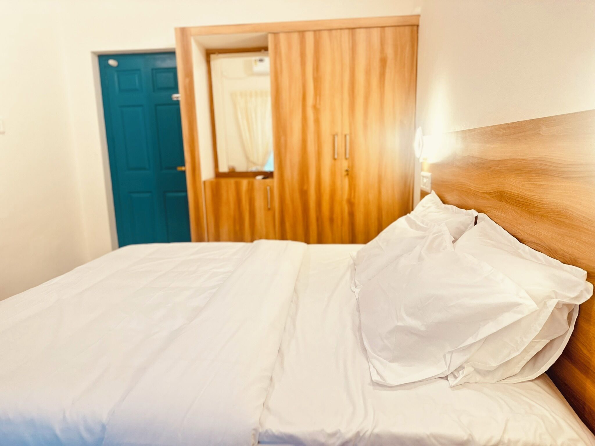Una cama bien hecha con sábanas blancas en una habitación con cabecera de madera y puerta azul.