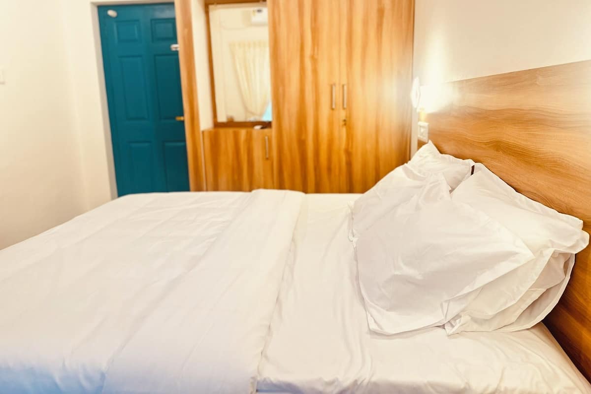 A neatly made bed with white linens in a room with a wooden headboard and a blue door.