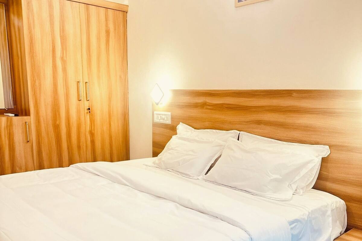 A neatly made bed with white linens in a room with wooden furniture and a small wall-mounted light.