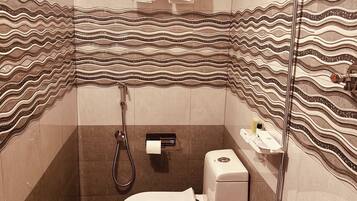 Et badeværelse med flisegulv, toilet, brusebad og et håndklædestativ med håndklæder.