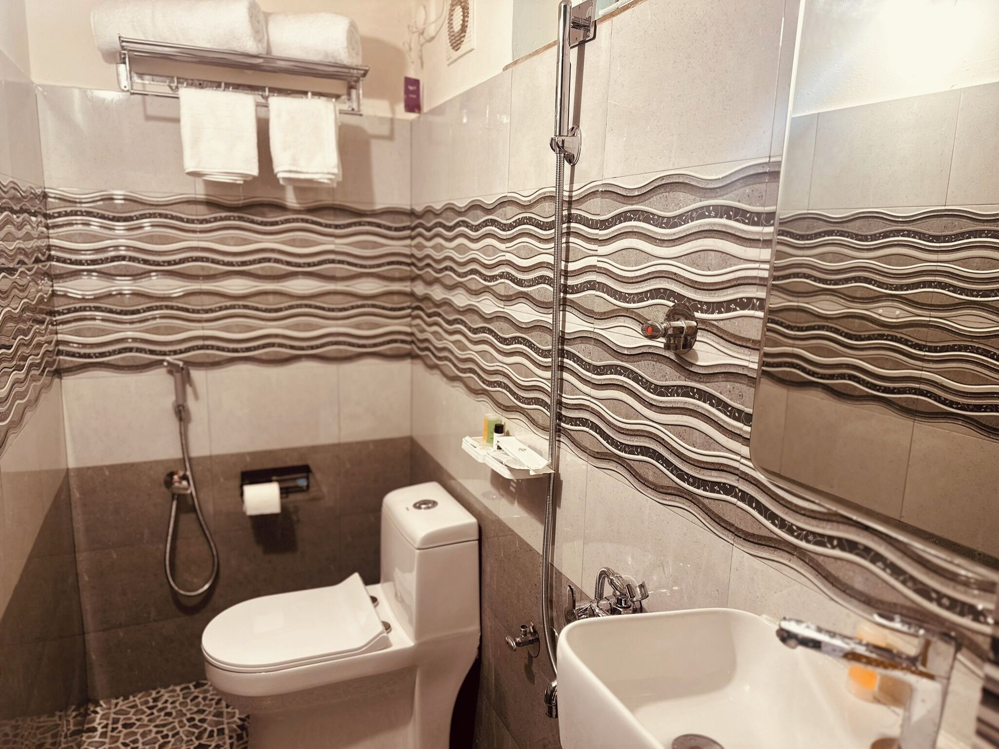 A bathroom with a toilet, sink, and shower. The walls have a wavy pattern design.