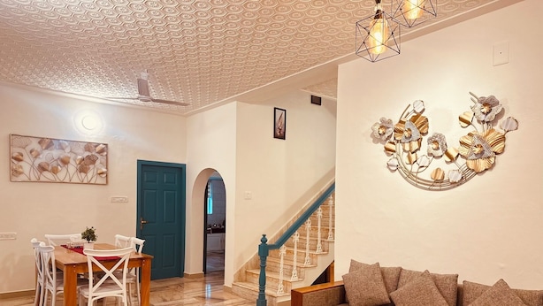 Un salon comprenant un canapé, une table basse, une table à manger avec des chaises, un escalier et des œuvres d’art décoratives murales.