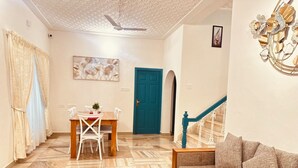 Un salon avec un canapé, une table basse avec des magazines, un coin repas avec une table et des chaises, et un escalier avec une rampe bleue.