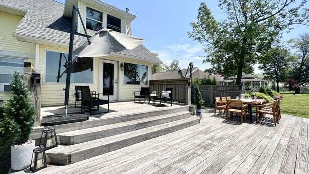 A wooden deck with outdoor furniture, a covered area, and a house in the background. - 5BR Sandy Pond MAIN LAKE HOUSE | Dock | Fire Pit | Pets (Sandy Creek)